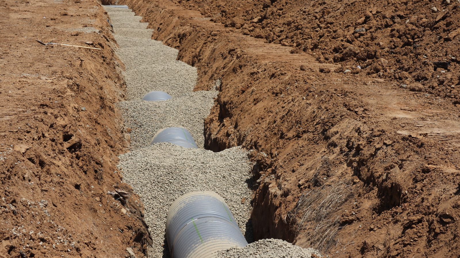 Perforated drain pipe bedded in washed stone inside an open trench